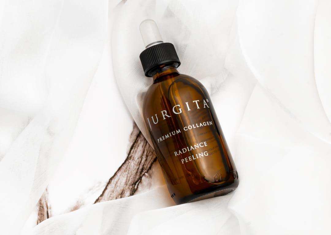 A luxurious amber glass bottle of "Radiance Peeling" lying on white fabric.