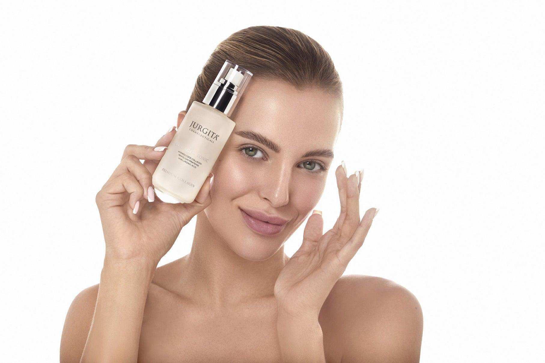 Smiling model with radiant skin holding the Jurgita Cosmeceuticals Collagen Tonic bottle, showcasing its premium packaging.