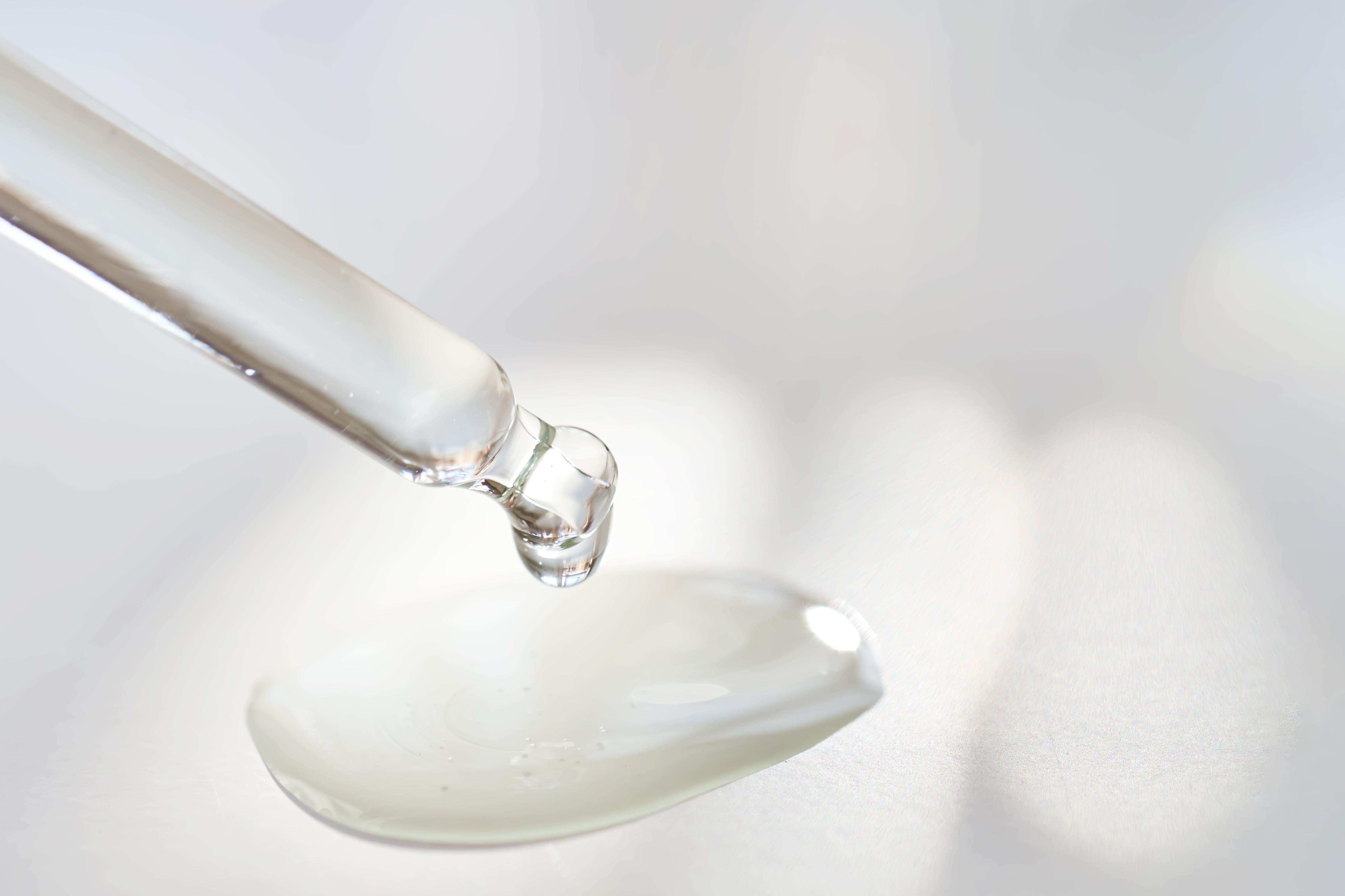 A transparent glass pipette dispensing a drop of Jurgita Cosmeceuticals Collagen Booster Sieroil, showcasing its lightweight, hydrating texture.