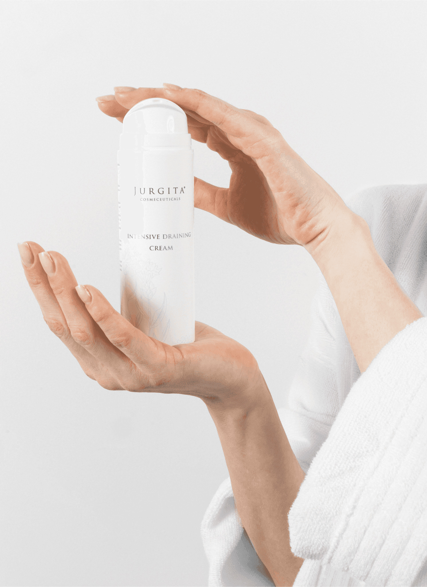 A woman in a white robe holding the Jurgita Cosmeceuticals Intensive Draining Cream, emphasizing its ability to promote lighter, smoother legs.