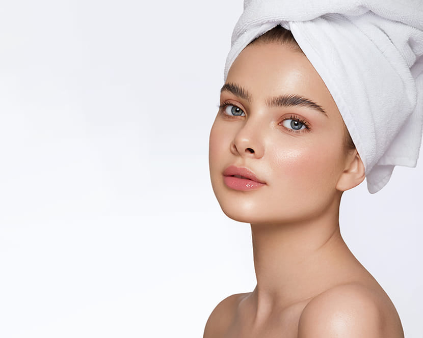 Woman with glowing skin and towel-wrapped hair, symbolizing luxury skincare results from Jurgita Cosmeceuticals by Wellskino.