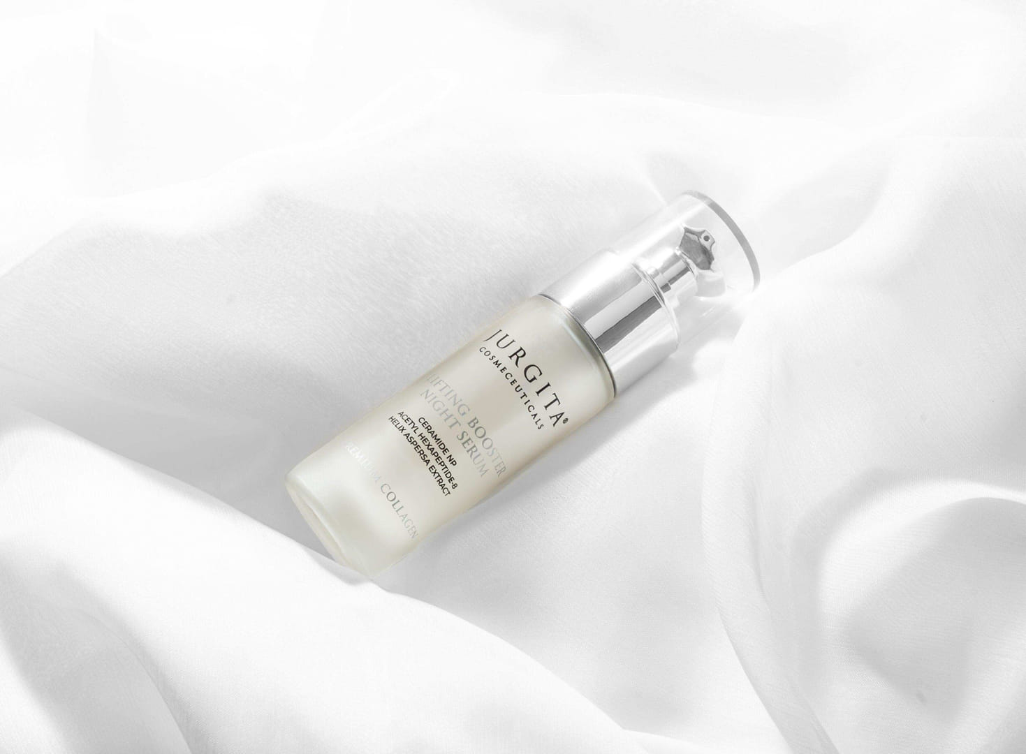 The Lifting Booster Night Serum bottle resting on soft white satin fabric, highlighting its elegance and high-end skincare appeal.