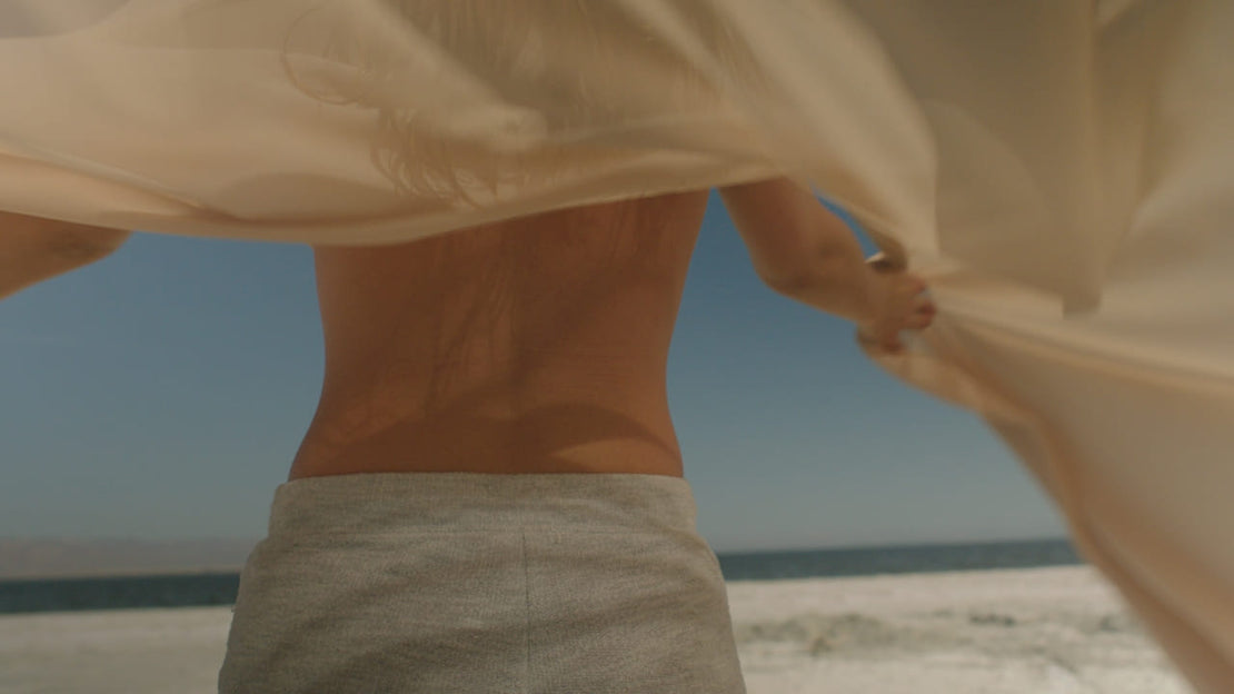 Woman standing at the beach with arms open, embracing natural light and movement — symbolizing freedom, authenticity, and self-acceptance.