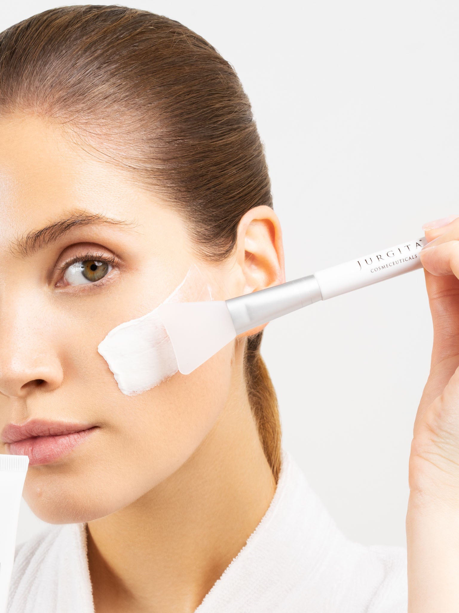 A woman wearing a soft white robe applies the Jurgita Zinc Rich Mask to her face, showcasing its creamy texture and deep hydration benefits.