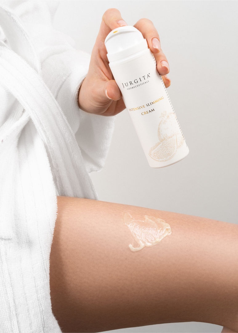 A person wearing a white bathrobe applying Jurgita Intensive Slimming Cream to their thigh, demonstrating the product’s smooth texture and ease of use.